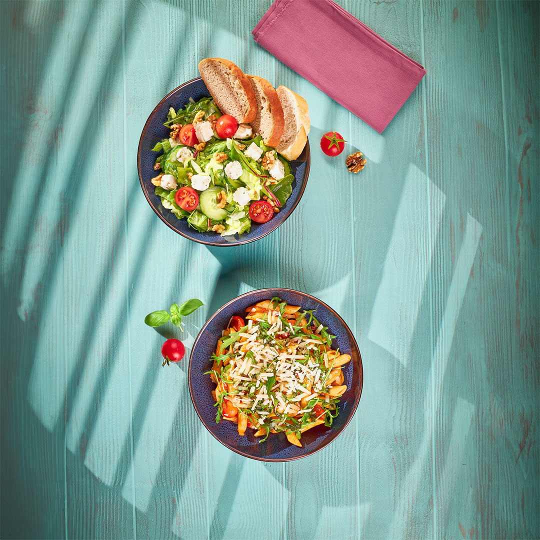 Zwei Teller mit Salat und Pasta auf einem Holzboden.